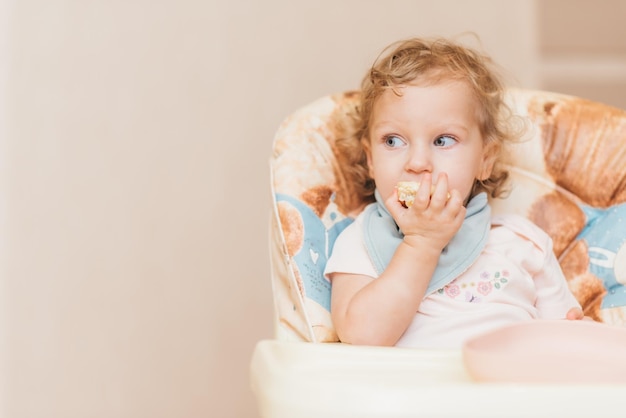 Happy little baby eats at home sitting on a chair