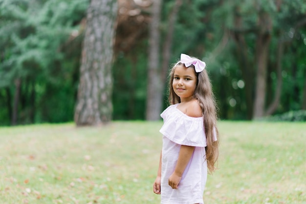 Happy little baby girl in a beautiful pink dress in the park on the grass and looking at the camera