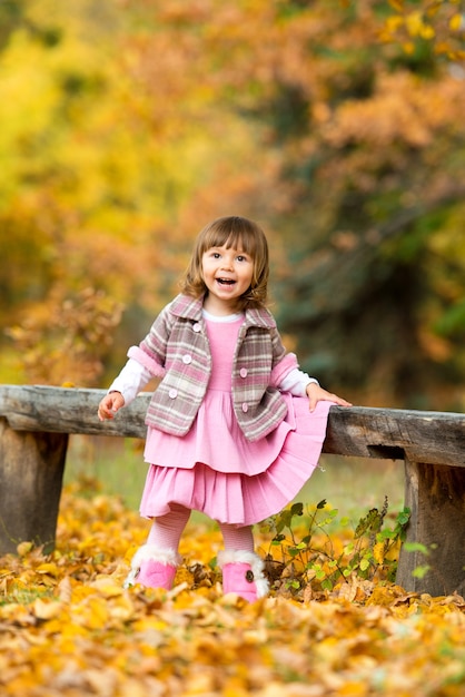 Happy little baby girl sitting on a bench laughing and playing with leaves. In nature, walk in the open air.