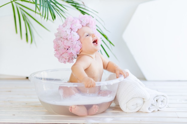 幸せな小さな女の赤ちゃんが泡と水で洗面器で洗う