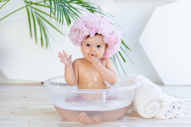 写真 幸せな小さな女の赤ちゃんが泡と水で洗面器で洗う