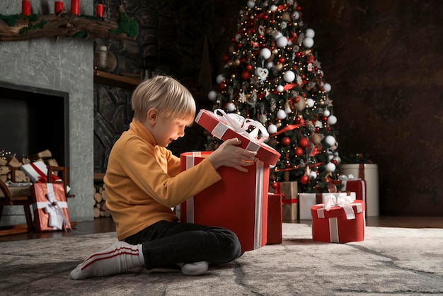 幸せな小さな金髪の少年は、子供のためのクリスマス プレゼントの内側から光るギフト ボックスに見えます
