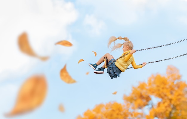 Foto felice piccola ragazza caucasica bionda sorride e cavalca su un'altalena in autunno