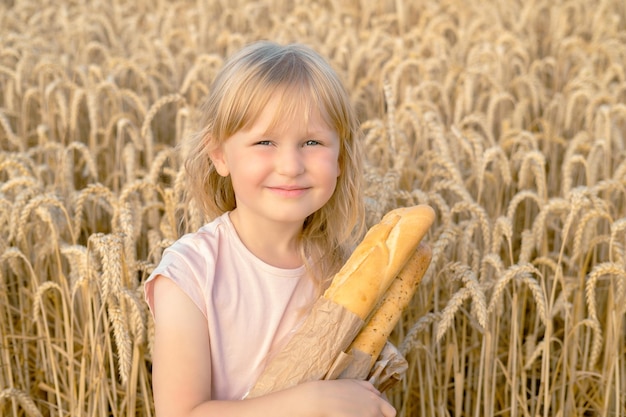 写真 小麦畑でフランスパンのバゲットを持った幸せなブロンドの女の子 パンを持つ子供たち