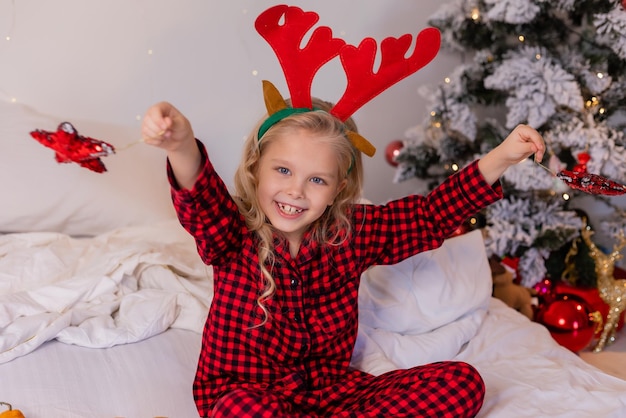 a happy little blonde girl in pajamas at Christmas looks at New Year's gifts and plays with New Year