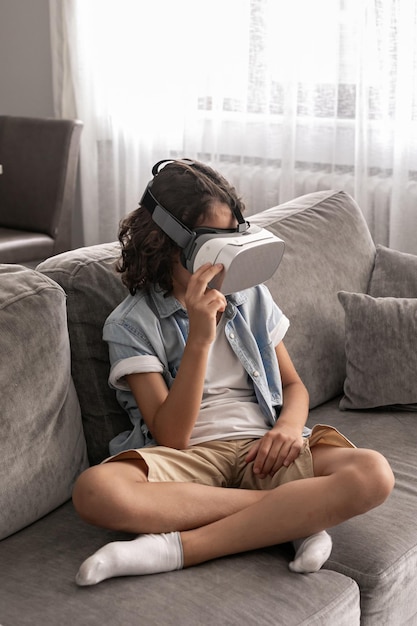 Happy little boy child using virtual reality headset vr glasses gesturing at home having fun