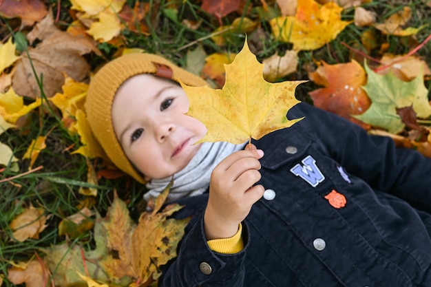 Happy little boy holding a maple leaf in his hand top view Boy have fun and lies on autumn leaves