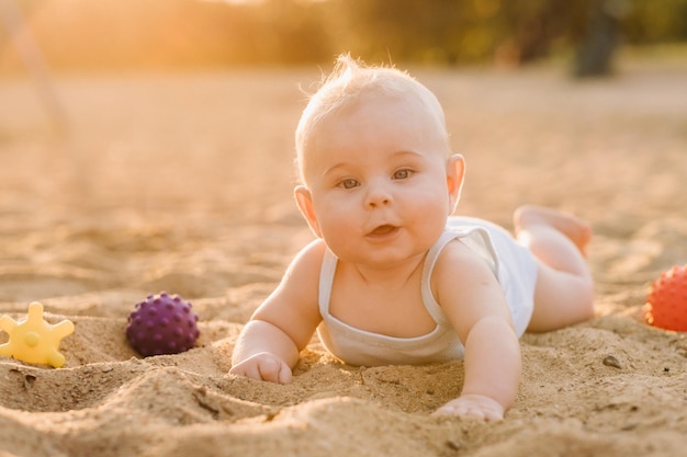 A happy little boy is lying on a sandy beach near the sea in the rays of the setting sun