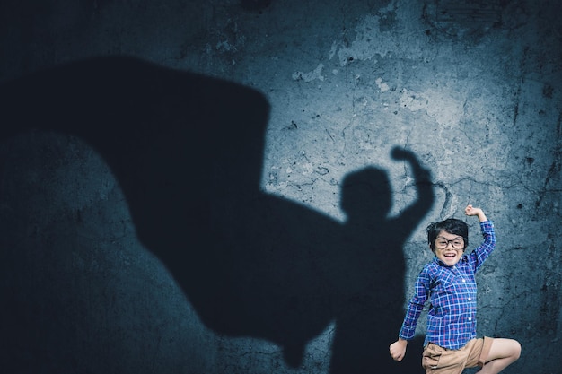 Счастливый маленький мальчик прыгает с тенью плаща супергероя