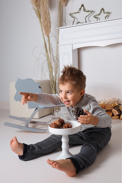 Foto ragazzino felice che gioca con le pigne. bambino che ride, decorazione di natale. celebrazione, tempo di natale.