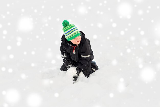 Счастливый маленький мальчик играет со снегом зимой