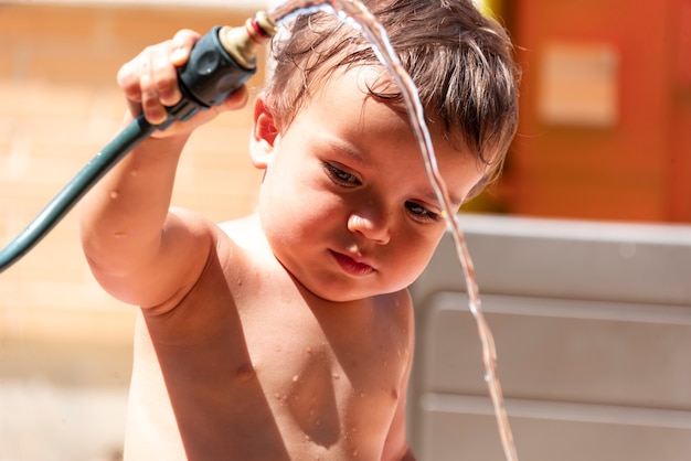 裏庭で水ホースで遊んで幸せな男の子