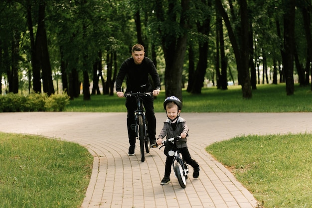 Happy little boy rides a bike with a young dad in the Park