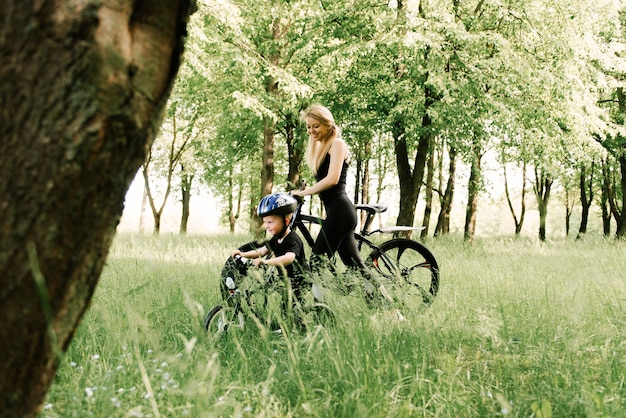 Happy little boy rides a bike with a young mom in the Park