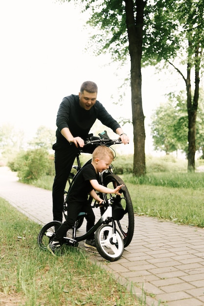 Happy little boy riding a bike with his dad in the park