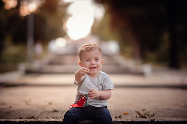Photo happy little boy sitting on street showing by hand