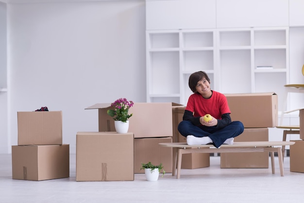 happy little boy sitting on the table with cardboard boxes around him in a new modern home