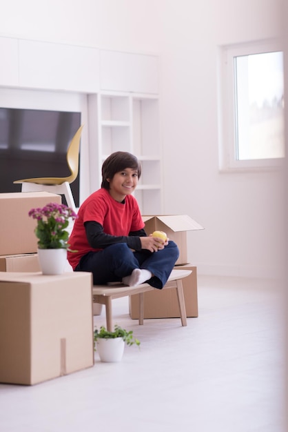 happy little boy sitting on the table with cardboard boxes around him in a new modern home