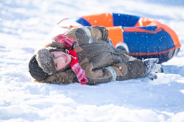 雪の滑り台でそりをする幸せな小さな男の子