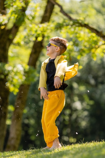 サングラスをかけた幸せな小さな男の子は、夏の公園でシャボン玉をキャッチします