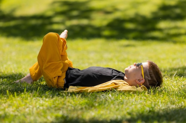 happy little boy in sunglasses lies on the lawn in summer