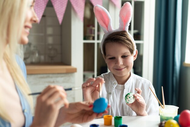 Happy little boy wearing in bunny ears preparing to Easter and painting eggs. Closeup portrait