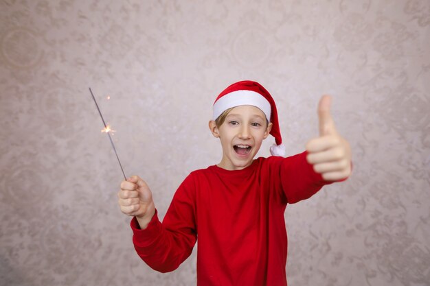 Photo happy little boy wearing santa hat and holding sparkler, new years eve