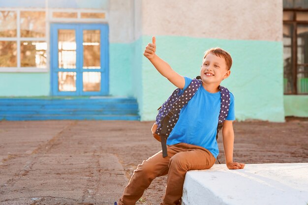 Happy little boy with backpack shows gesture of victory