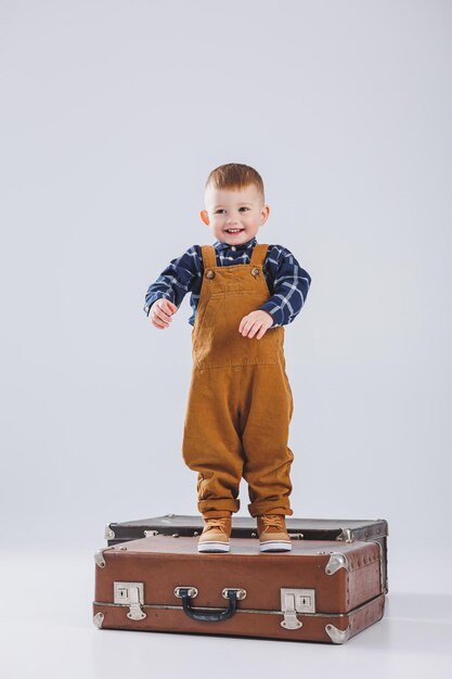 Happy little boy with a brown suitcase Portrait of a child tourist a child in overalls Little traveler with a suitcase