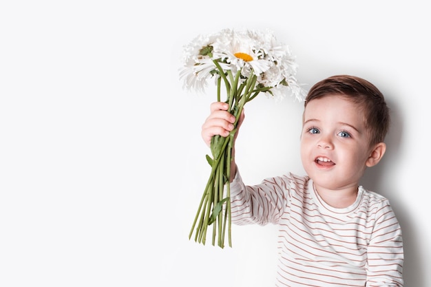 白い背景にデイジーの花を持つ幸せな小さな男の子、かわいい笑顔の子供は夏に楽しんでいます