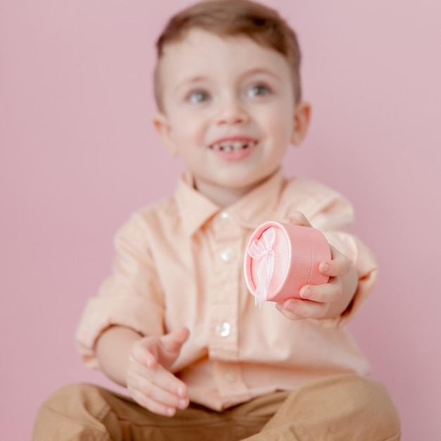 Happy little boy with a gift Photo isolated on pink background Smiling boy holds present box Concept of holidays and birthday