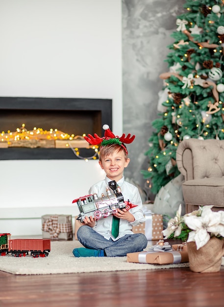 새해 아침에 크리스마스 트리 아래에서 선물 장난감 기차를 가지고 있는 행복한 어린 소년