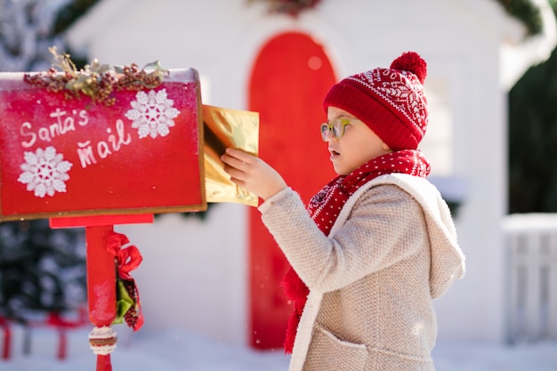 Happy little boy with red hat and green glasses sending her letter to Santa, Christmas time