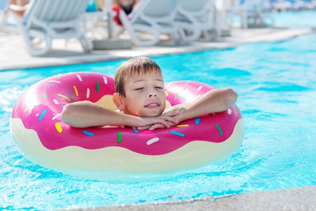 Happy little boy with variegated life ring in the form of a donut
 has fun in the swimming pool