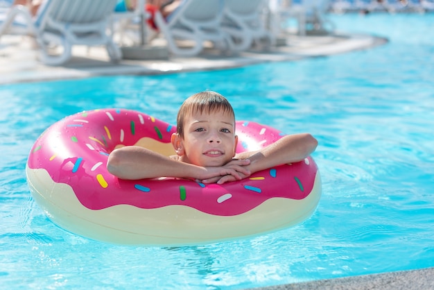 Happy little boy with variegated life ring in the form of a\
donut has fun in the swimming pool