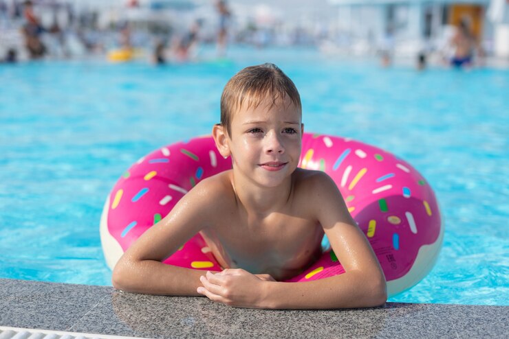 Happy little boy with variegated life ring in the form of a donut
 has fun in the swimming pool