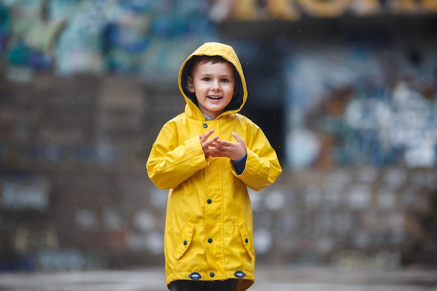 Happy little boy in a yellow raincoat close up.