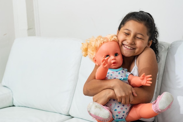 Happy little brunette girl with the doll her parents just gave her hugging her doll tightly