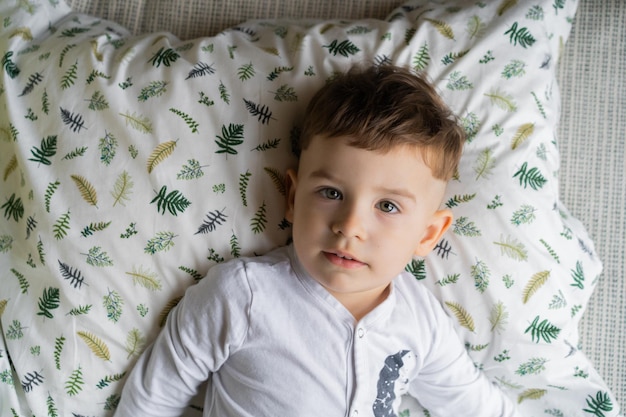 Happy little child boy in pajamas, in bed in the bedroom with toys, plays, sleeps. Beautiful baby bedding. Children's daytime sleep. Soft light.