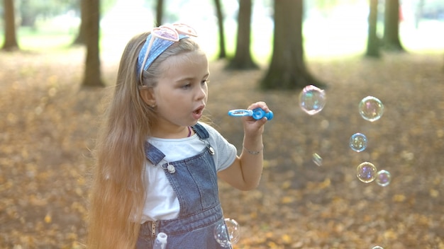 Happy little child girl blowing soap bubbles outside in green park. Outdoor summer activities for children concept.