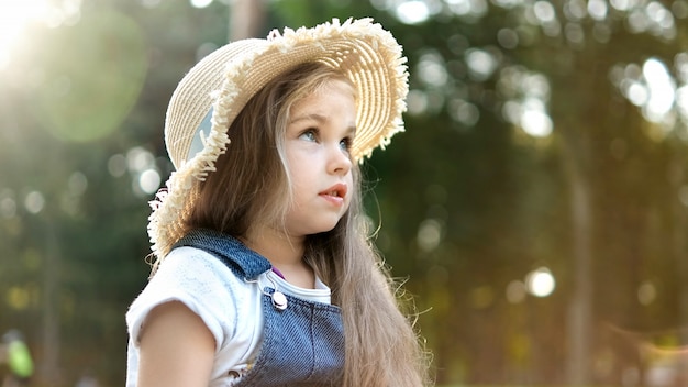 Happy little child girl in straw hat outdoors.