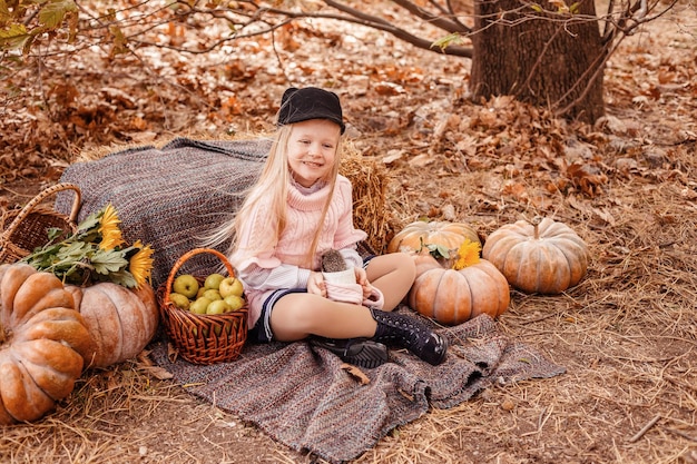 Happy little child girl with cute hedgehog Portrait of kid with pet in autumn nature with pumpkins and straw holding a cup of hot drink