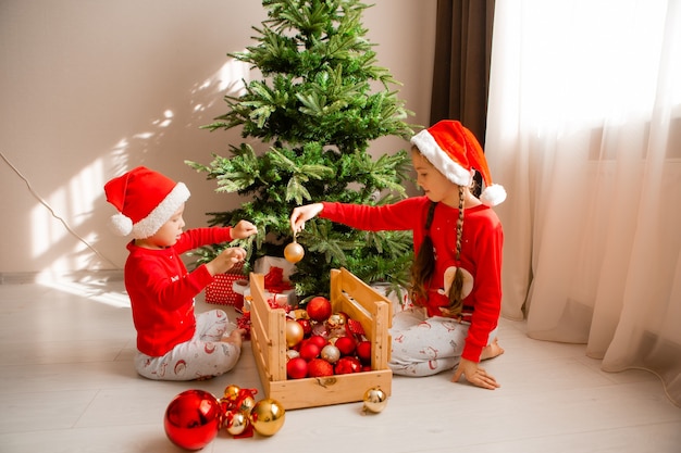 happy little children in red pajamas are decorating a Christmas tree in living room winter concept