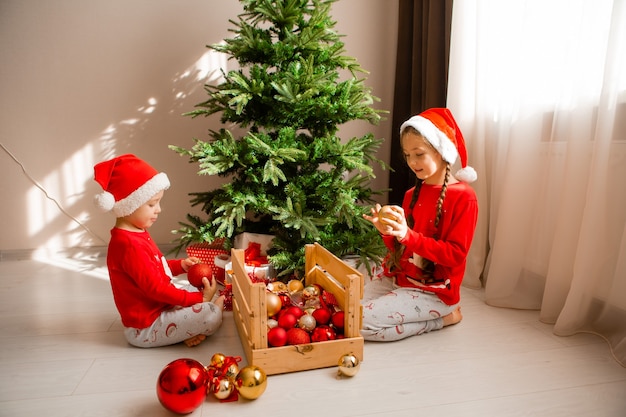 happy little children in red pajamas are decorating a Christmas tree in living room winter concept