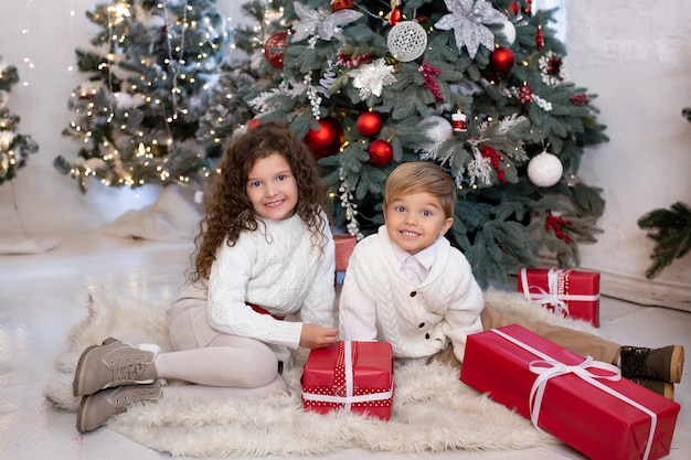 Happy little children with gift boxes in their hands near Christmas tree and light