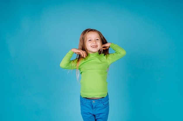 幸せな小さなかわいい子の女の子は青い背景で隔離の手を上げて笑顔