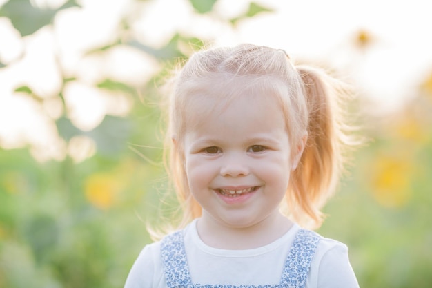 Happy little girl 3 years old in a sunflower field in the sun Cute child holding a flower in his hands Summer