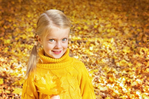 Happy little girl in autumn park with yellow maple leaves in her hands.