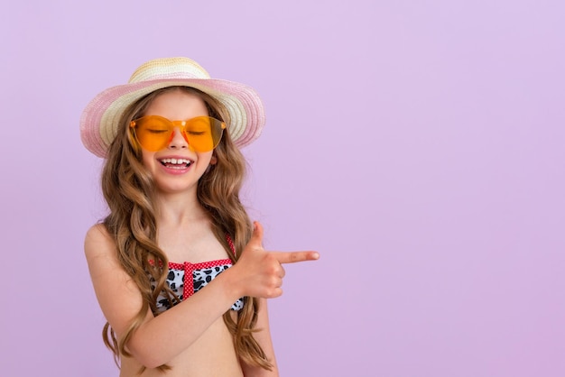 A happy little girl in a bathing suit and sunglasses points her finger to the side Isolated background