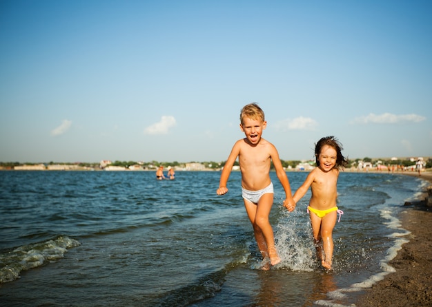 Happy little girl and boy running on water edge in sunshine